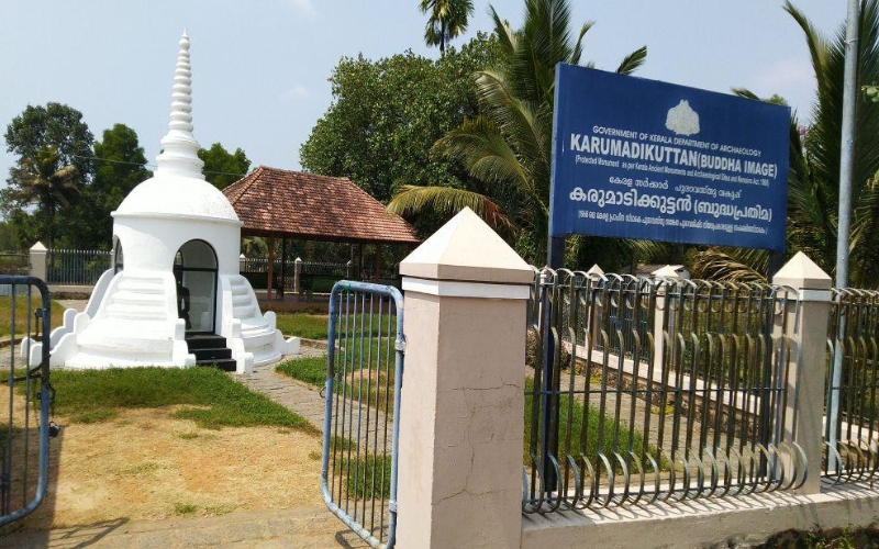 A historic black granite statue of Karumadikuttan, an ancient Buddha idol located in Alappuzha, Kerala, surrounded by lush greenery.